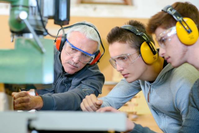 Two young men being instructed by a man in woodworking