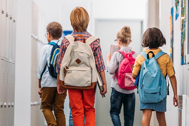Young Children wearing school backpacks walking down a corridor
